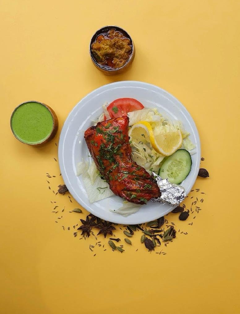 Authentic Indian tandoori chicken leg garnished with fresh herbs, served with salad and green chutney